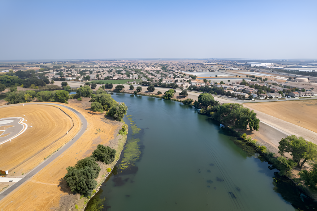 An expansive aerial view of Lathrop, California, featuring a winding river, tree-lined streets, and houses in a peaceful suburban setting.