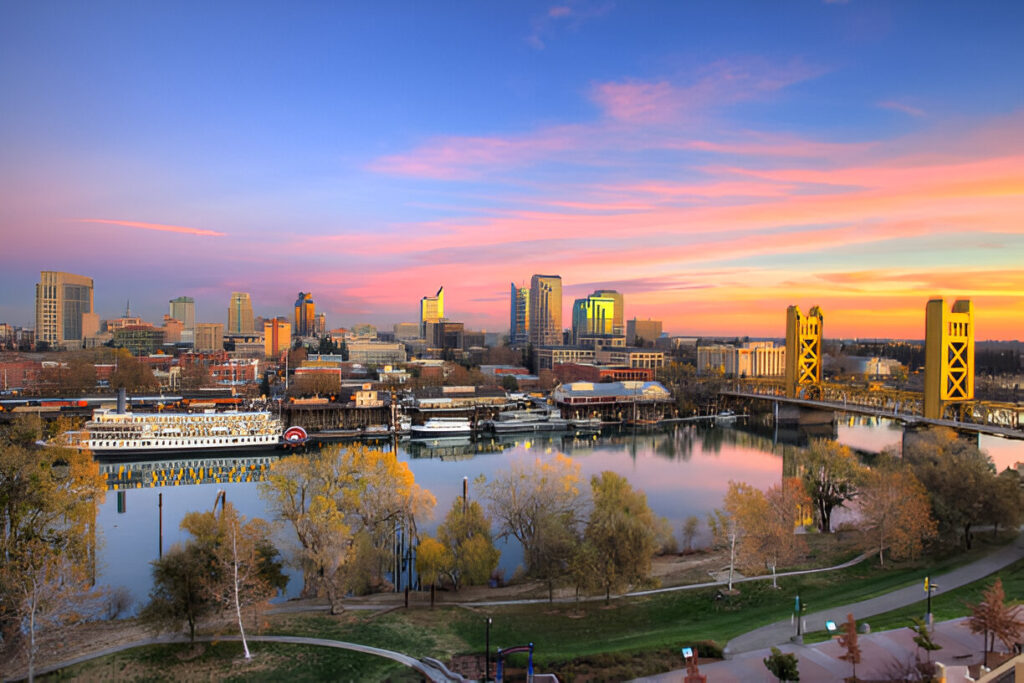 Sacramento, CA, aerial riverfront view with a bridge, skyline, and boats, showcasing the city's vibrant real estate market.